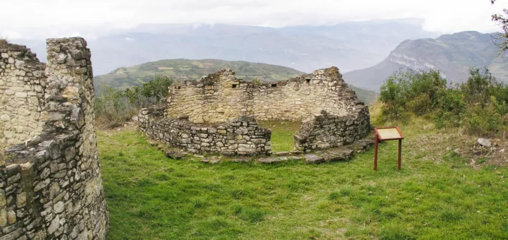 Ruinas circulares de piedra sobre el césped en la fortaleza de Kuélap, con las montañas de Amazonas al fondo