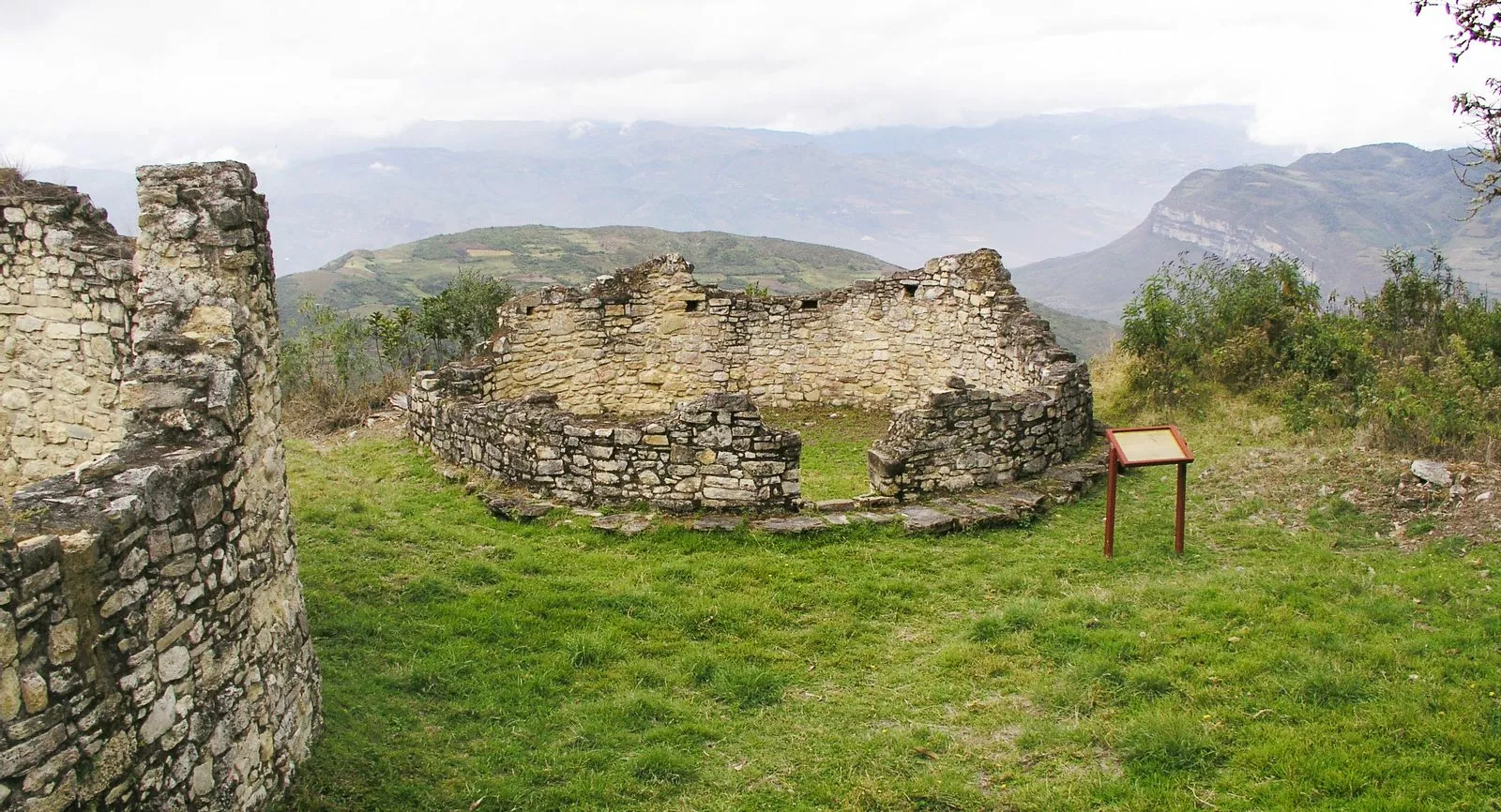 Ruinas circulares de piedra sobre el césped en la fortaleza de Kuélap, con las montañas de Amazonas al fondo
