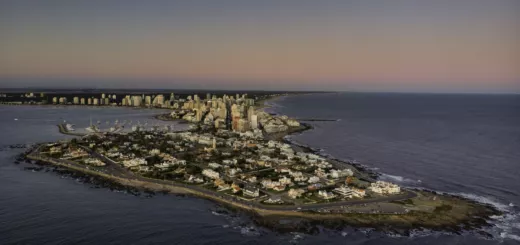 Vista aérea de la península de Punta del Este al atardecer, con edificios junto a la costa y el mar oscuro alrededor