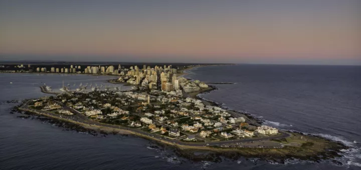 Vista aérea de la península de Punta del Este al atardecer, con edificios junto a la costa y el mar oscuro alrededor