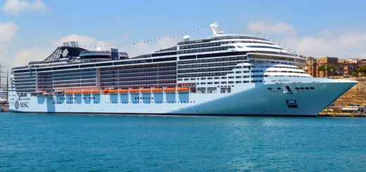 Crucero MSC Divina de casco blanco amarrado en un puerto, con la ciudad de piedra al fondo y cielo azul