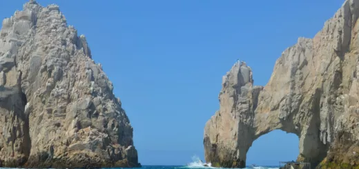El Arco de Cabo San Lucas entre dos farallones de roca sobre el mar azul, con una lancha de pasajeros al frente