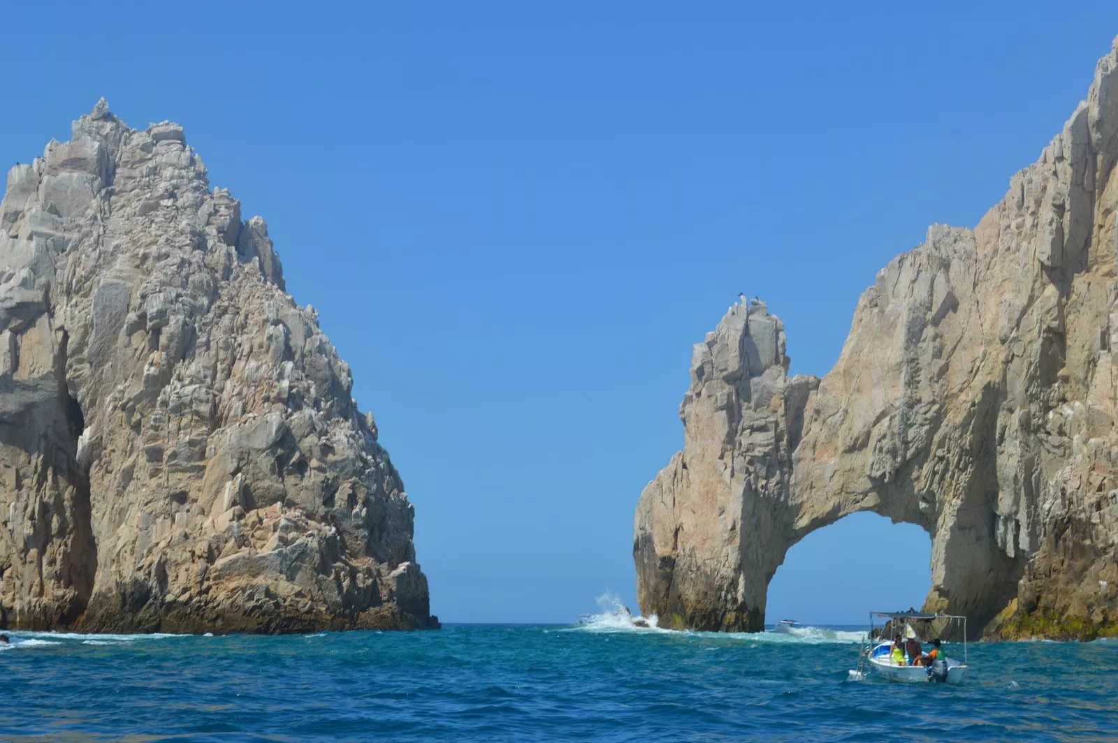 El Arco de Cabo San Lucas entre dos farallones de roca sobre el mar azul, con una lancha de pasajeros al frente